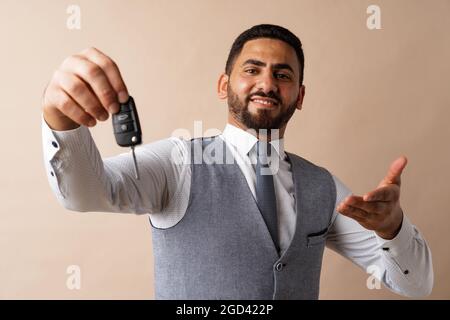 Young arab guy holding a car key and showing it against beige background Stock Photo