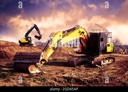 Digger working against a dramatic sky with another digger on the hill in the background Stock Photo