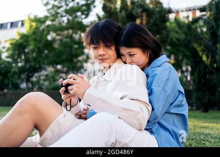 Cute asian couple sitting in the park together and using a camera. Stock Photo