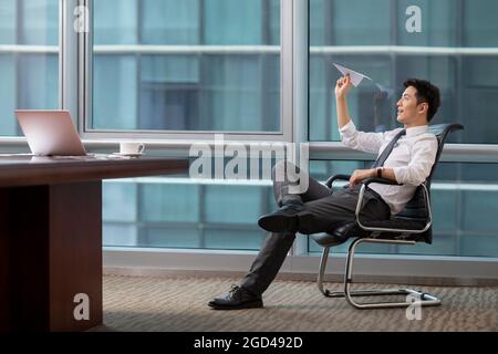 Confident businessman throwing paper plane in office Stock Photo