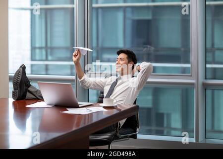 Confident businessman throwing paper plane in office Stock Photo