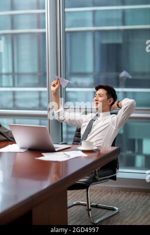 Confident businessman throwing paper plane in office Stock Photo