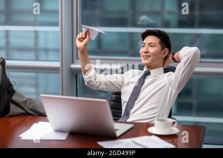 Confident businessman throwing paper plane in office Stock Photo