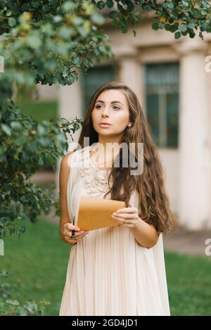 A romantic young woman in a summer dress holds a vintage letter in her hands Stock Photo