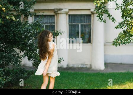 A young woman with long hair runs through the grass in the city park in summer, her hair fluttering in the wind. Stock Photo