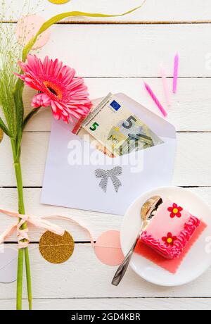 Euro money as birthday gift concept. Euro bank notes inside of envelope, decorated with cake and flowers. Stock Photo