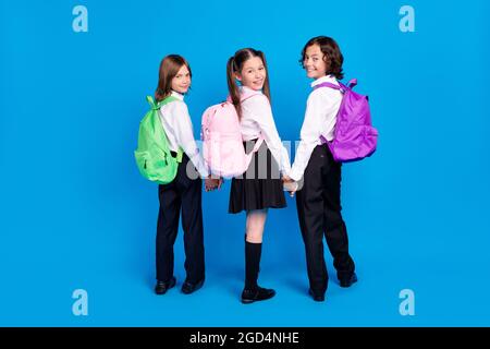 Photo of pretty adorable schoolchildren wear uniform rucksacks holding arms walking smiling isolated blue color background Stock Photo