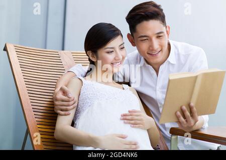 Happy pregnant woman and husband reading a book Stock Photo