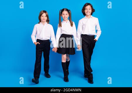 Photo of sweet shiny schoolchildren wear uniform holding arms walking smiling isolated blue color background Stock Photo