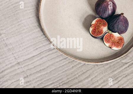 Autumn breakfast in bed composition. Blank greeting card mockup, cup of coffee and fig fruit on ceramic plate. White linen background. Velvet cushions Stock Photo