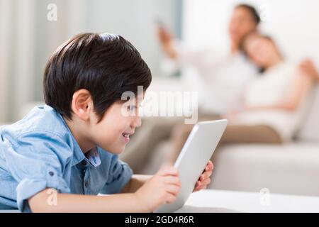 Happy boy playing digital tablet with parents in background Stock Photo