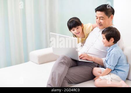 Happy grandfather and grandchildren using laptop at home Stock Photo