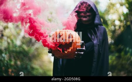 Girl with Halloween costume and make up holding pumpkin with a smoke bomb inside - Focus on hands holding pumpkin Stock Photo