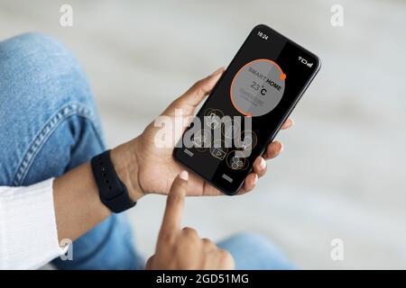 Black woman hands regulating air conditioner at apartment via smart home mobile application on smartphone, cropped. Female setting room temperature, u Stock Photo