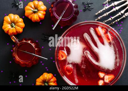 Happy Halloween party flat lay composition. Bowl with frozen hands, bloody drinks, strawberries and pumpkins, cocktails, bony hands on dark background Stock Photo