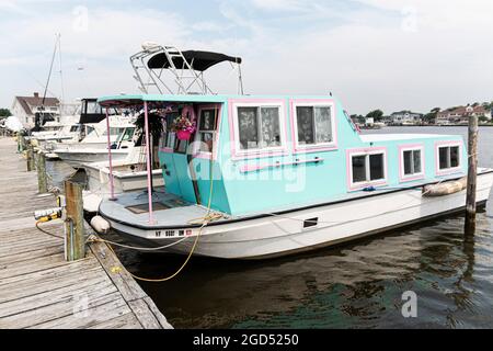 Babylon, New York, USA - 29 June 2019: A houseboat pugged into the electric moored at a dock painted with tropical colors. Stock Photo