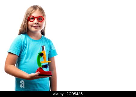 Portrait of a cute little girl in round glasses and a toy microscope in her hands on a white background. A schoolboy works with a microscope. Smart ki Stock Photo