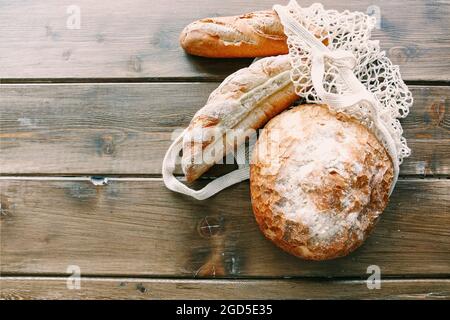 Top view of three loaves of different varieties of freshly bought bread lies in white grocery mesh bag on wooden vintage rustic style table surface. N Stock Photo