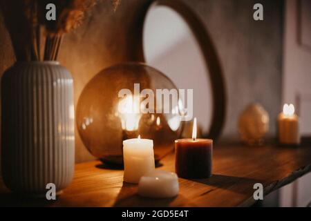 Round mirror on wooden shelf with two burning candles and small porcelain Buddha head reflected in corner of mirrored surface over concrete wall backg Stock Photo