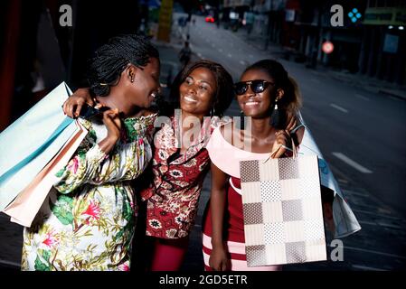 group of young women standing outdoors laughing while holding shopping bags. Stock Photo