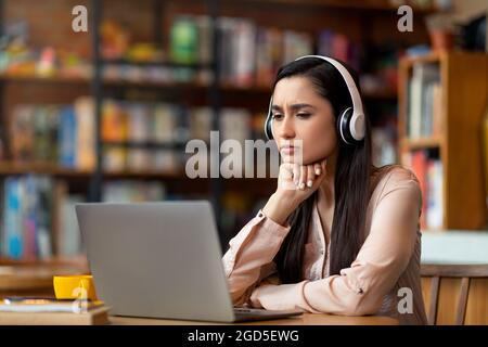 Online education concept. Concentrated latin woman studying online at cafe, using laptop and headset, copy space. Arab female student having online le Stock Photo