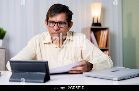Businessman checking tax or contract papers and noting down from internet using tablet at office - concept of paper work, e-learning and modern workin Stock Photo
