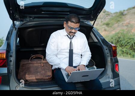 Young businessman working from the car trunk or boot near roadside - concept of digital nomadic lifestyle, travel freelancer and vacations. Stock Photo