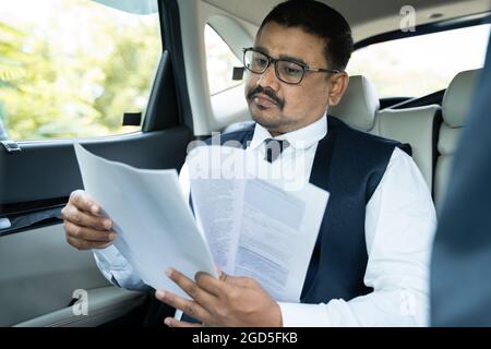 young businessman reading project documents while traveling in car - Concept of successful happy people Stock Photo