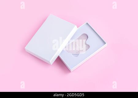 Rose quartz natural stone Gua Sha face massager in white packaging box top view Stock Photo