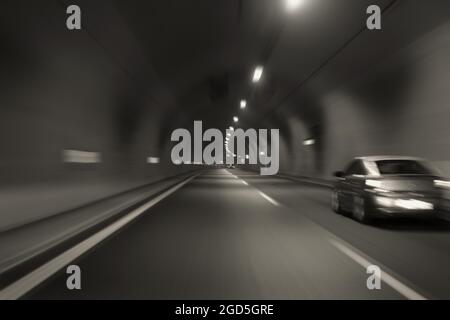 Car speeding through motorway tunnel motion blur. Black and white tint long exposure. Stock Photo