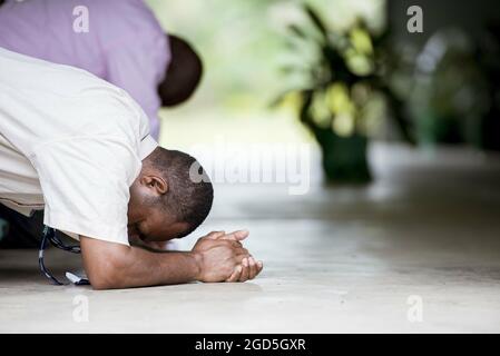 PORT MORESBY, PAPUA NEW GUINEA - May 06, 2018: A closeup shot of a dark skinned man praying on the ground with his hands combined Stock Photo