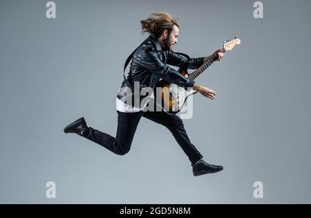 emotional bearded rock musician playing electric guitar in leather jacket and jumping, music Stock Photo