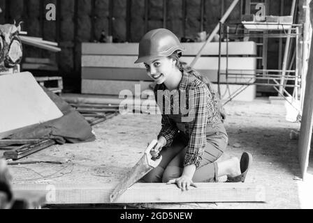 girl working with wood in workshop. carpentry and woodwork concept. Portrait of a cute kid posing as a carpenter, with a handsaw. working as Stock Photo