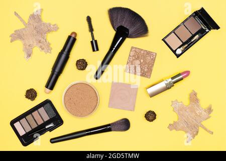 Autumn make-up flat lay. Makeup products brown, bronze, gold colors with fall decorations on yellow background. Top view Stock Photo