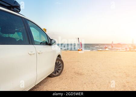 Side view of big family white suv van car with big rooftop cargo rack box at scenic sand seaside campsite camp coast of sea or ocean sky on background Stock Photo