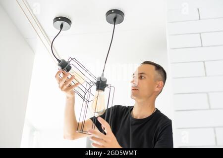 Worker repairing lamp on stretch ceiling indoors Stock Photo