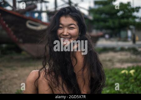 Portrait of smiling charming asian girl. Brunette with long curly hair posing. Looking at camera with copy space. Wind in her hair. . High quality  Stock Photo
