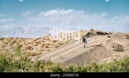 rear view of an asian man backpacker photographer walking on a dirt road through gobi desert Stock Photo