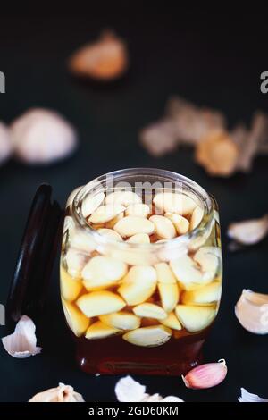 Fermented garlic cloves in a jar of honey, a rich source of  probiotics, over a rustic wood background table. Selective focus with blurred background Stock Photo
