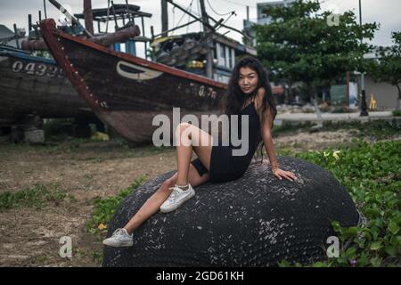 Sitting on the stone near old wooden ships. Brunette long curly hair. Looking at camera with copy space. Romantic photo. High quality photo Stock Photo