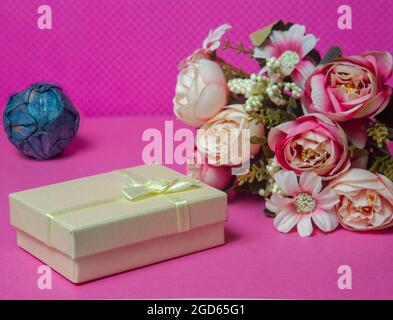 Photo of a bouquet of flowers, beige gift in the form of a box on a pink background front view. High quality photo Stock Photo