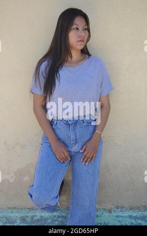 A south asian young girl posing with wearing gray tshirt and blue jean standing against yellow wall with looking sideways Stock Photo