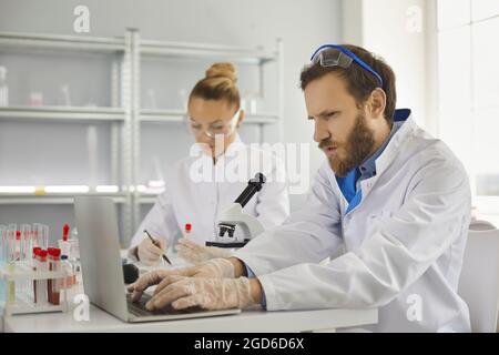 Concentrated scientist typing laptop keyboard working on research report in lab Stock Photo