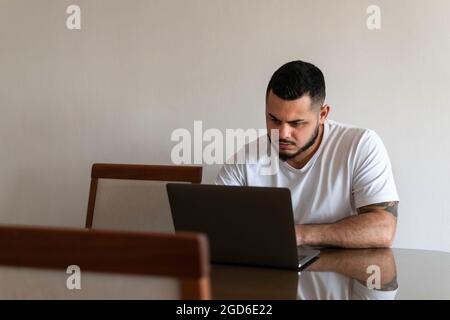 Latino man looking with an angry face at a laptop screen Stock Photo
