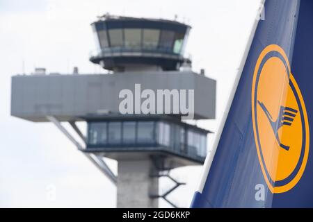 10 August 2021, Brandenburg, Schšnefeld: The logo on the tail unit of a Lufthansa aircraft can be seen against the backdrop of the tower at Berlin Brandenburg Airport 'Willy Brandt'. Photo: Soeren Stache/dpa-Zentralbild/dpa Stock Photo