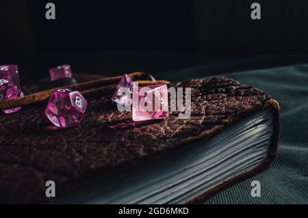 Close-up image of pink transparent role-playing gaming dice on top of a brown leather-bound book lit by a ray of sunlight Stock Photo
