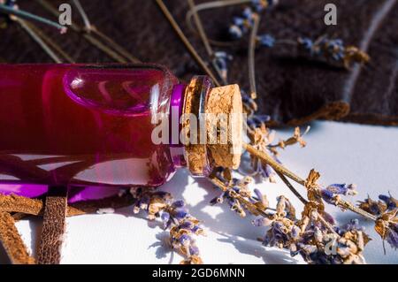 Close-up image of a glass stopper bottle with pink liquid and dried lavender on an open notebook. Stock Photo