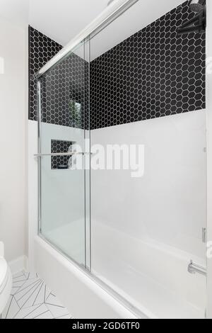 A shower with small black hexagon and large white hexagon tiles in a shower. The floor is also a patterned black and white tile. Stock Photo