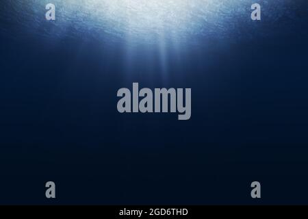 Dark blue ocean surface seen from underwater. Abstract waves underwater and rays of sunlight shining through. Stock Photo