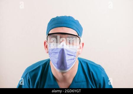 Young doctor with fogged glasses in blue surgeon suit and medical mask on yellow background isolated. Stock Photo